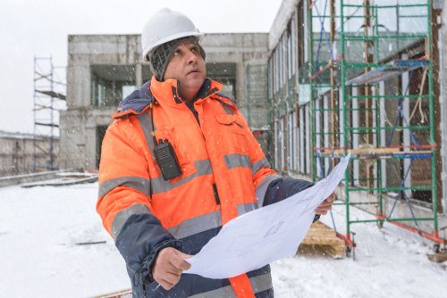 a construction worker holding a sheet of paper and looking at a scaffolding system in the snow