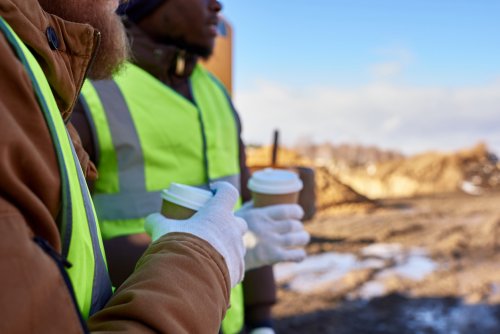 two construction workers drinking hot drinks to warm themselves up
