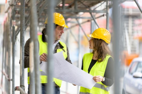 two male and female construction workers talking under scaffolding